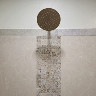 Showerhead centered above a decorative tile strip on a beige-tiled wall.