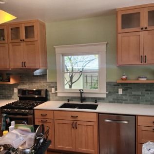 Kitchen with light wood cabinets, stainless steel appliances, and green backsplash.