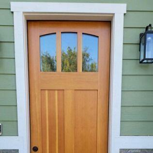 Wooden door with arched top windows and white trim against green siding.