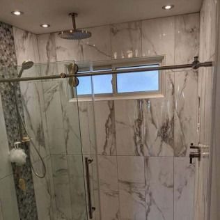 Shower with glass door, marble-like tile walls. Chrome hardware. Window.