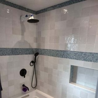 White tiled shower with blue mosaic trim, black showerhead, and a built-in shelf.