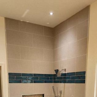 Shower with light beige and teal tile, showerhead, and recessed lighting.