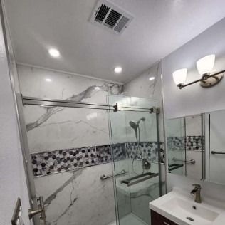 Modern bathroom with marble walls, glass shower, and mosaic tile accent.