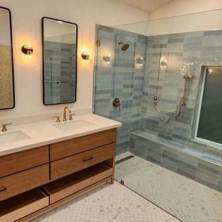 Bathroom with wooden vanity, two mirrors, tiled shower, and glass door.