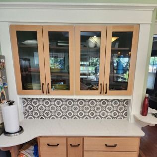 Light wood kitchen cabinets with glass doors, patterned backsplash, and countertop.