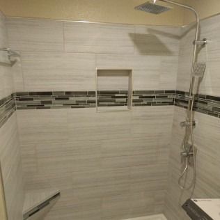 Shower tiled in light gray with a decorative band, recessed shelf, and silver shower fixtures.