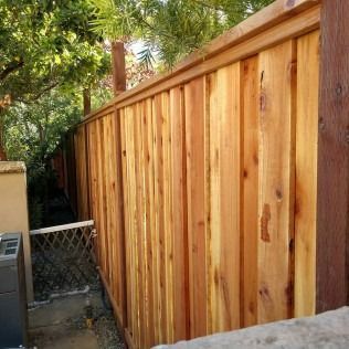 Wooden fence, cedar planks, brown with a decorative top rail, outdoor setting.