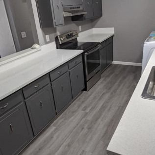 Grey kitchen cabinets with white countertops and a stainless steel oven. Gray flooring.