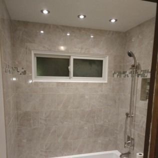Bathroom with beige tiled walls, a window, shower head, and recessed lighting.