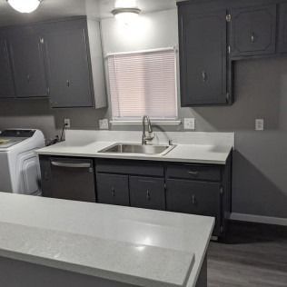 Kitchen with gray cabinets, a white countertop, and a stainless steel sink.