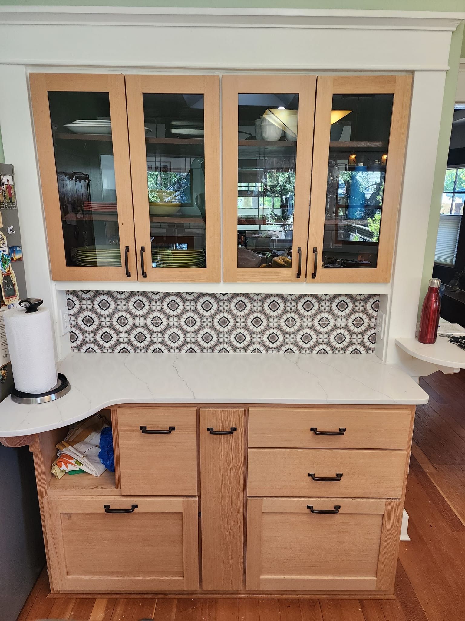 Kitchen hutch with wood cabinets, glass doors, tile backsplash, and white countertop.