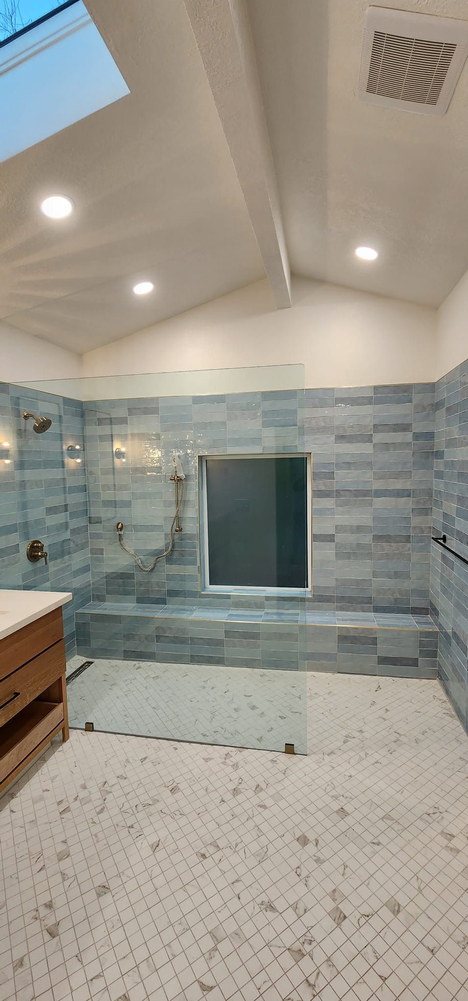 Spacious bathroom with gray tiled shower and white floor. Recessed lighting in the high ceiling.