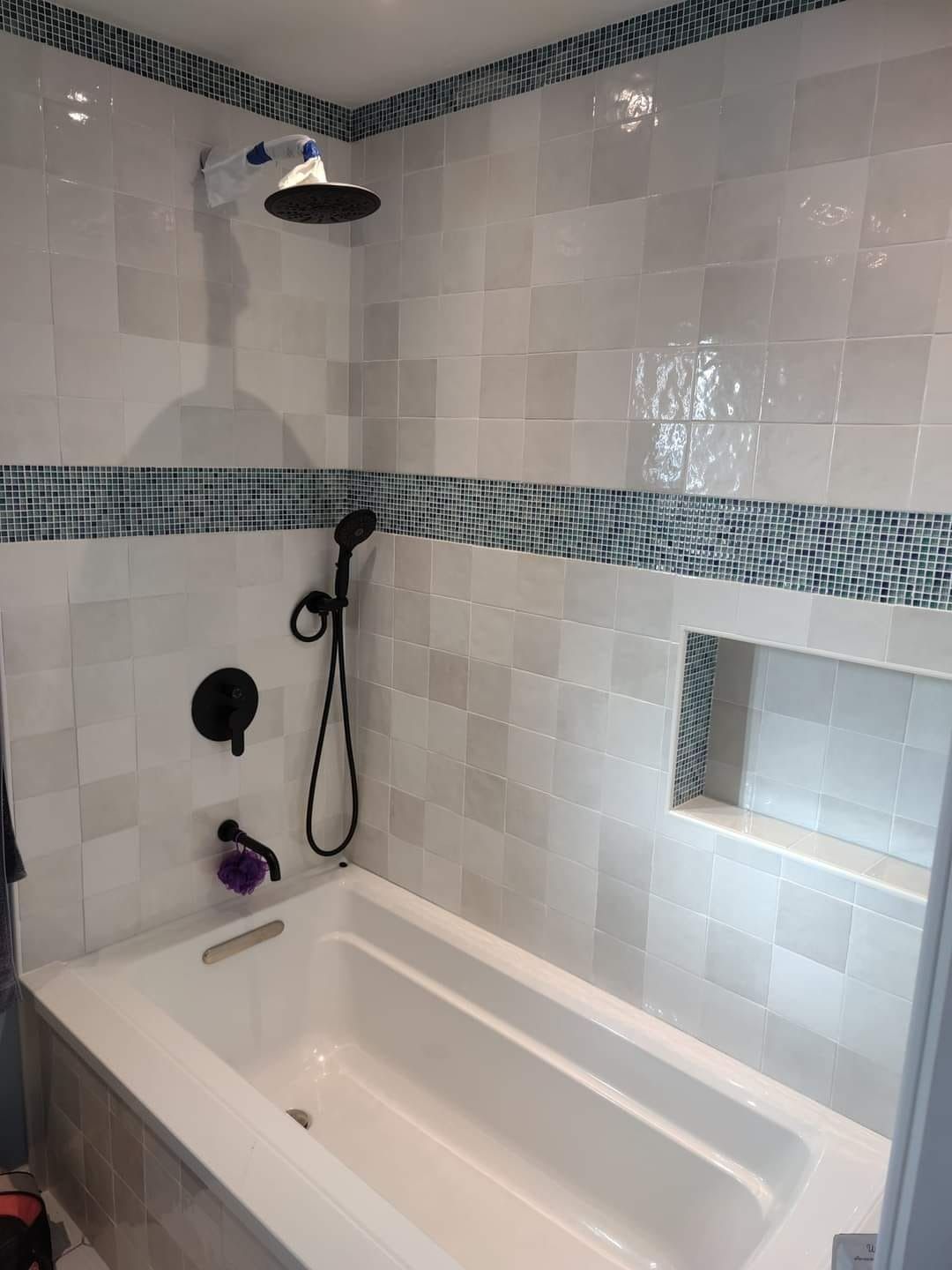 Bathroom with white and blue tile, black fixtures, and a bathtub.