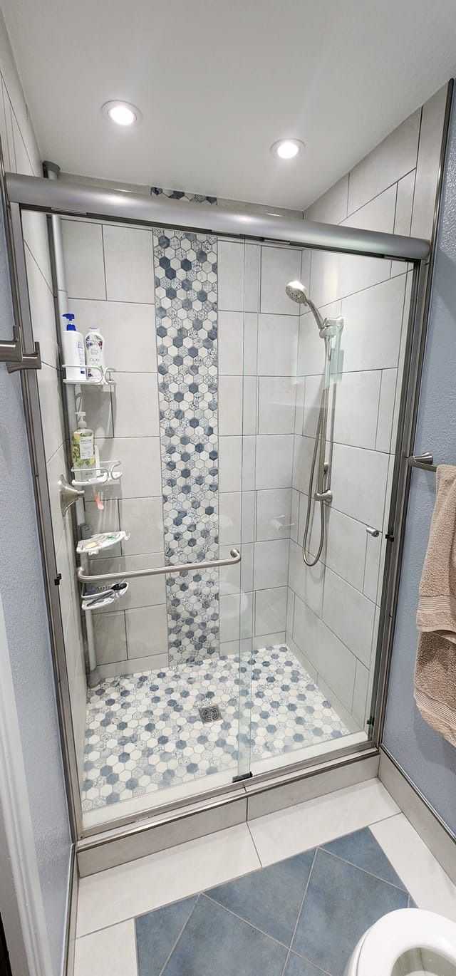 A small, tiled shower with a glass door, mosaic accents, and a shower head.