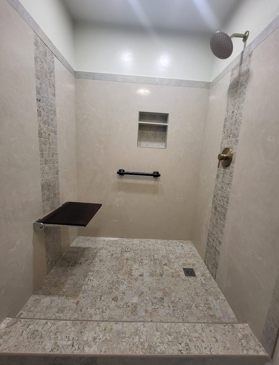 Accessible shower with built-in seat, grab bar, and recessed shelf. Light-colored walls and speckled floor.