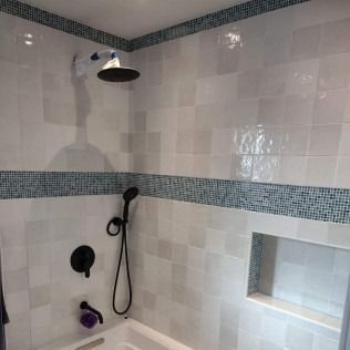 White tiled shower with blue mosaic border and black fixtures.