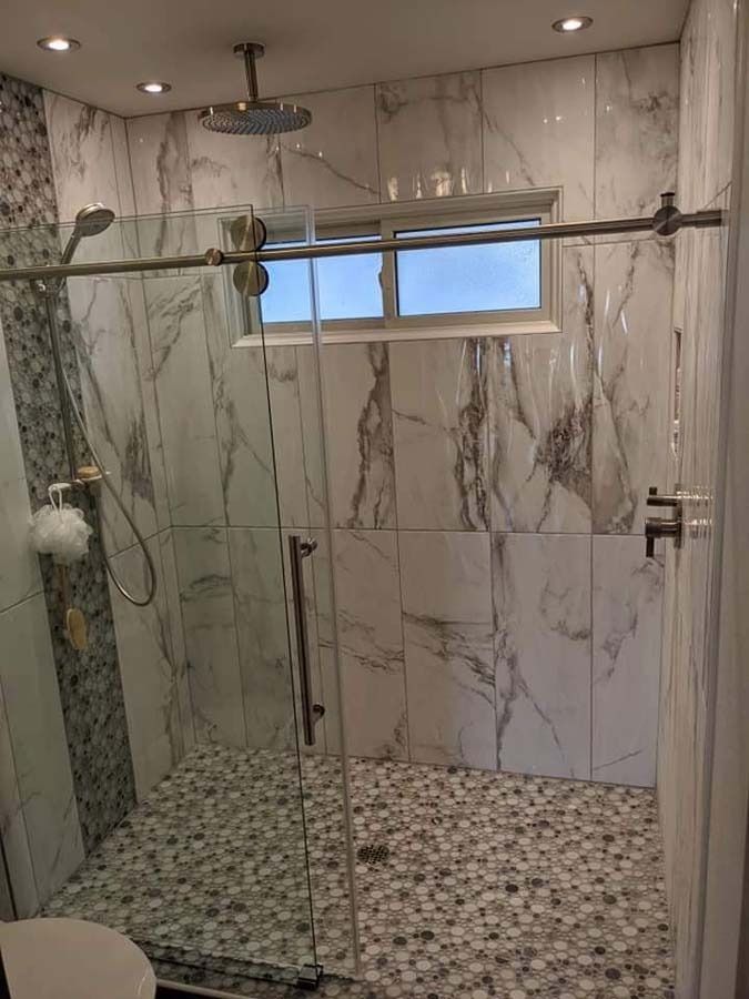 Modern shower with marble-like tile walls and pebble floor. Glass door and window. Chrome fixtures.