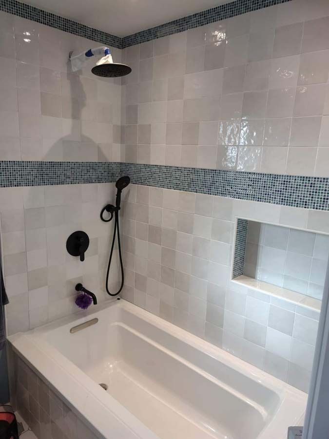 Bathroom with white tiled walls, blue mosaic accent, and black fixtures. Bathtub and showerhead are visible.