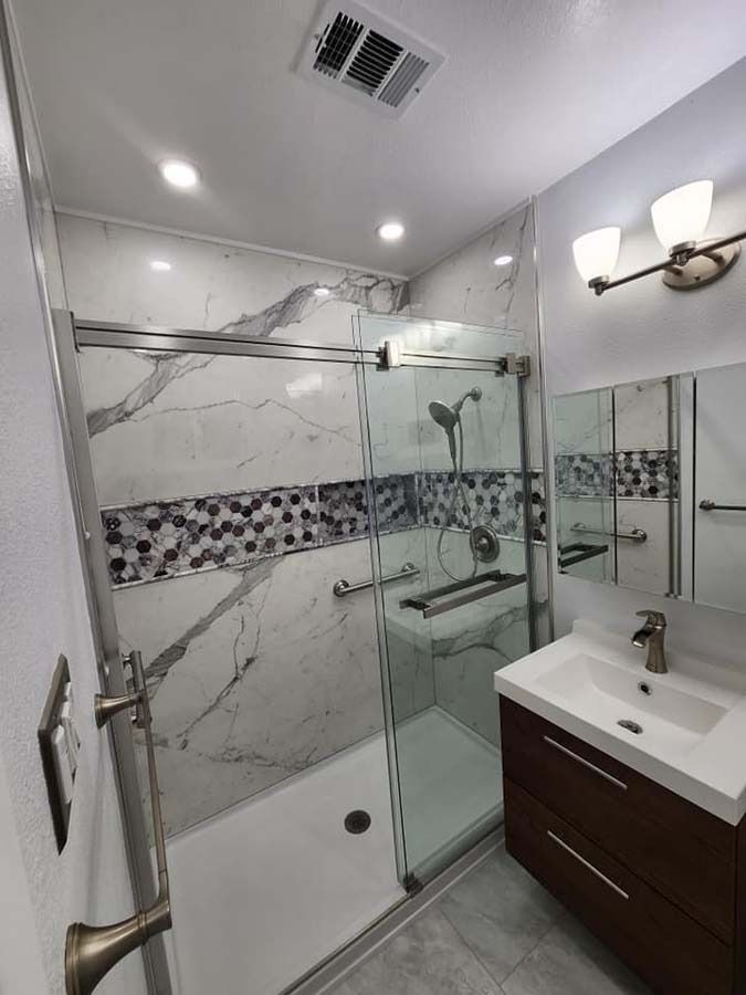 Modern bathroom with a marble-tiled shower, glass door, vanity, and a decorative tile band.