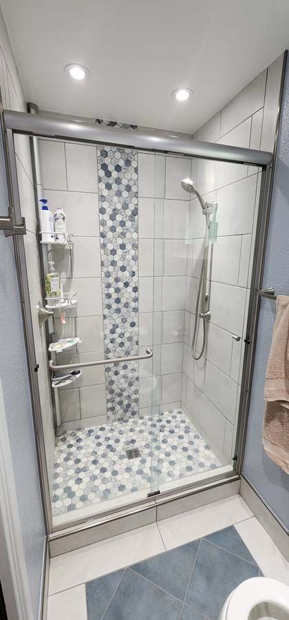 Shower stall with glass door, mosaic tile accents, and built-in shelving.