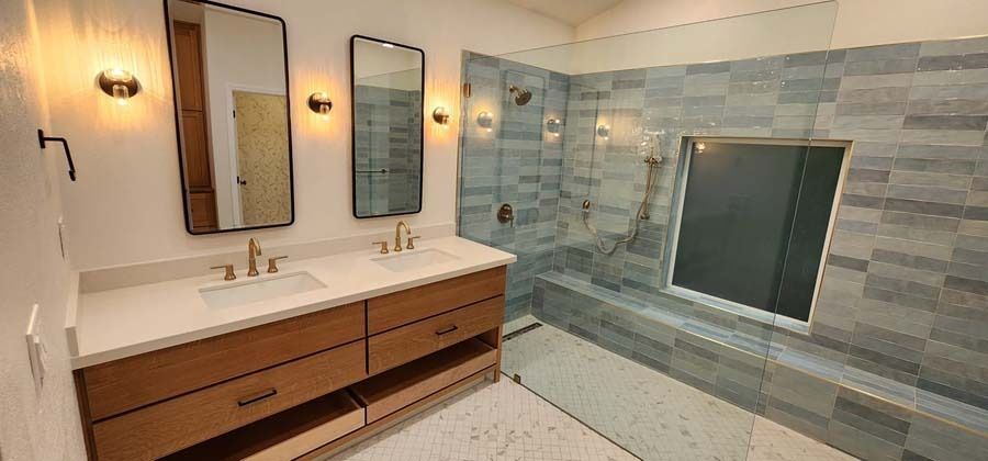 Modern bathroom with double vanity and tiled shower, featuring mirrors, lights, and wood cabinetry.