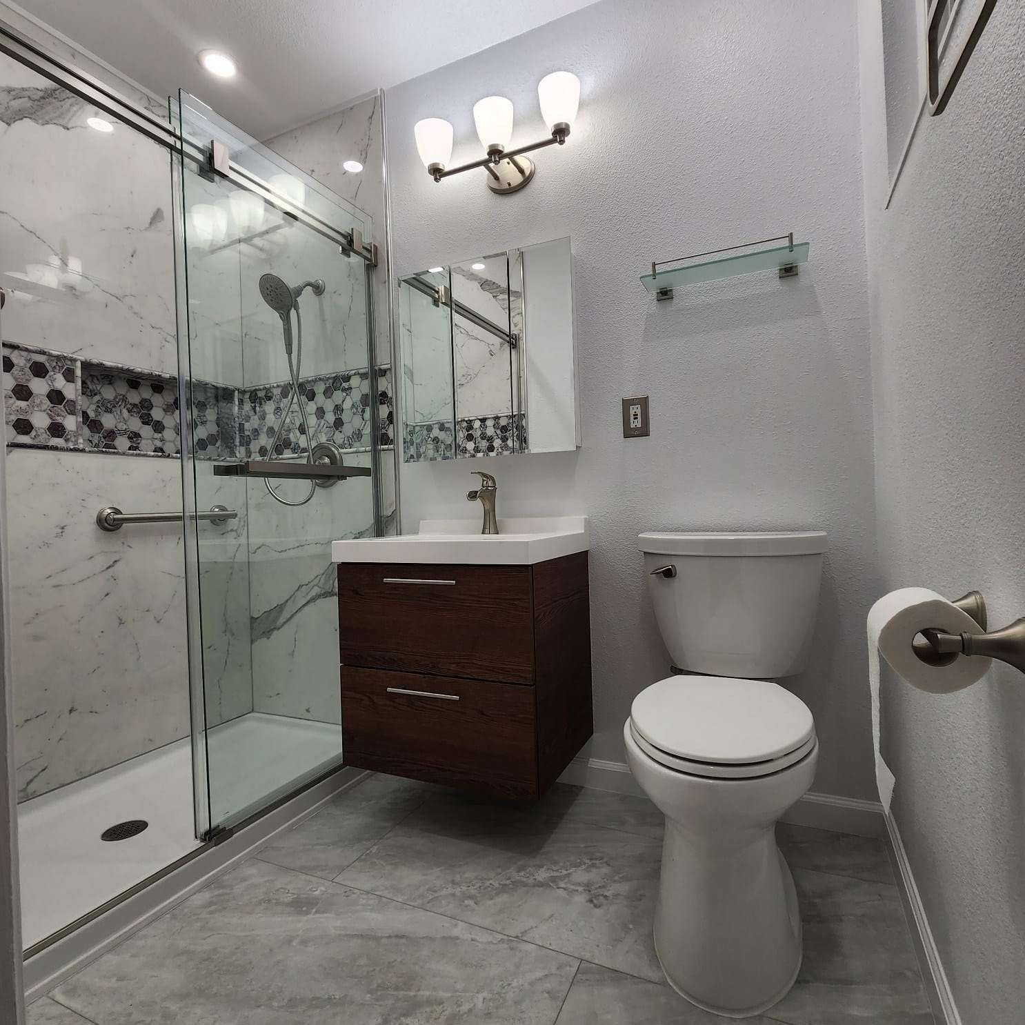 Bathroom with shower, vanity, toilet, and gray tiled floor and walls.