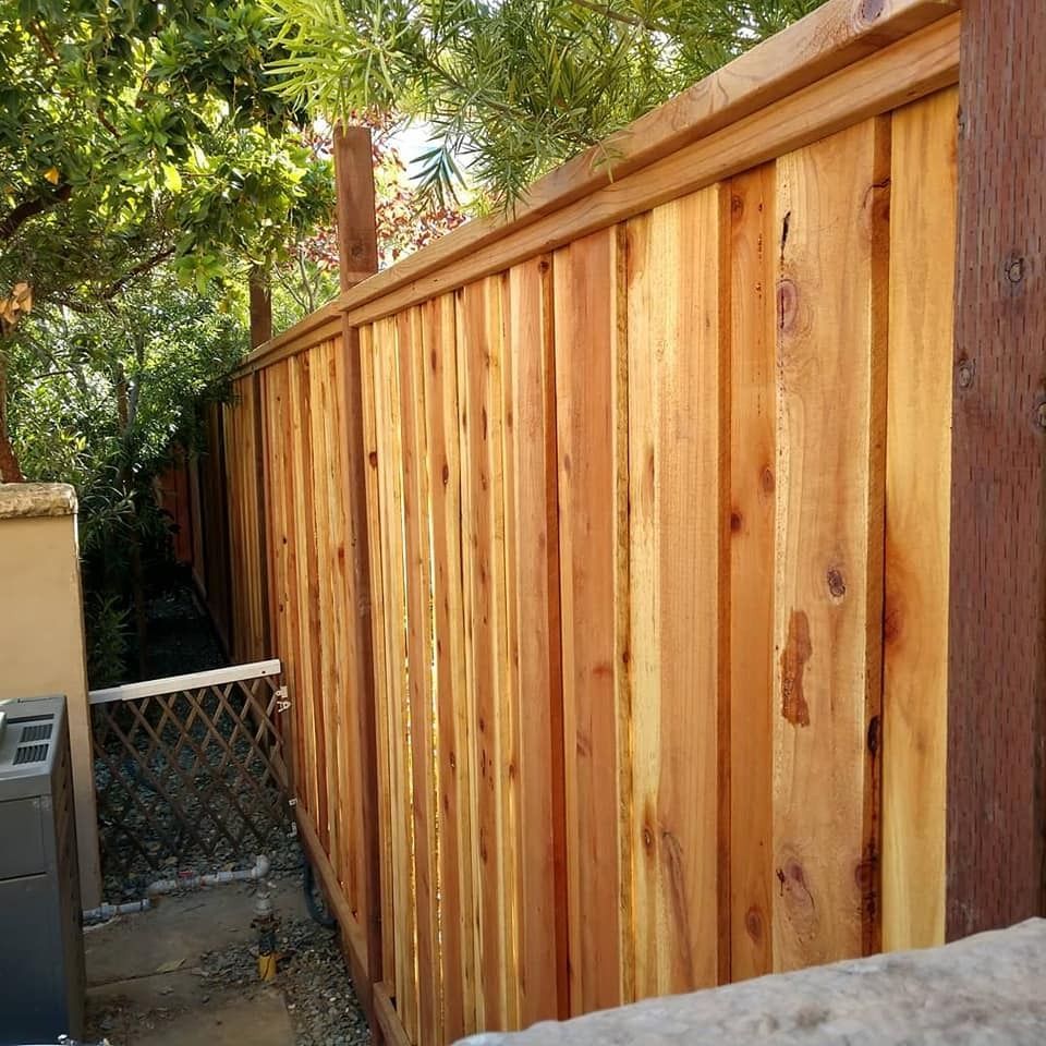 Wooden fence in natural wood tone with cap, enclosing a yard with greenery.