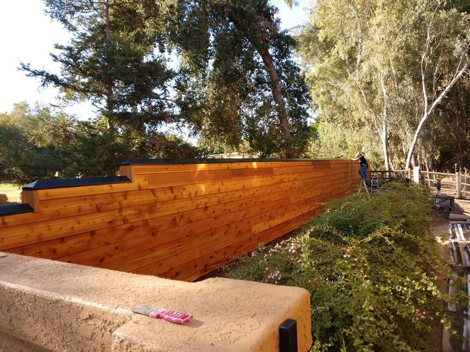 Wooden retaining wall with greenery and trees in the background; person working.