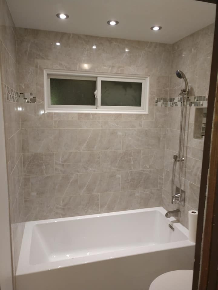 Bathroom with a white bathtub, gray tiled walls, and a small window.