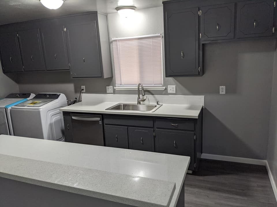 Gray kitchen with cabinets, sink, and island; a washer and dryer are visible.