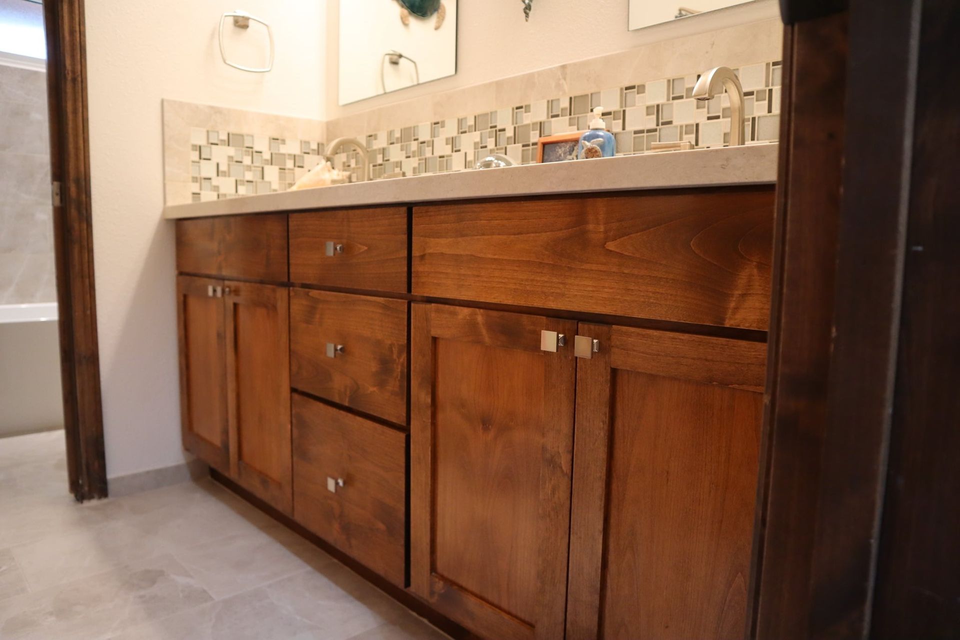 Wooden bathroom vanity with drawers and cabinets, neutral-colored countertop, and decorative backsplash.