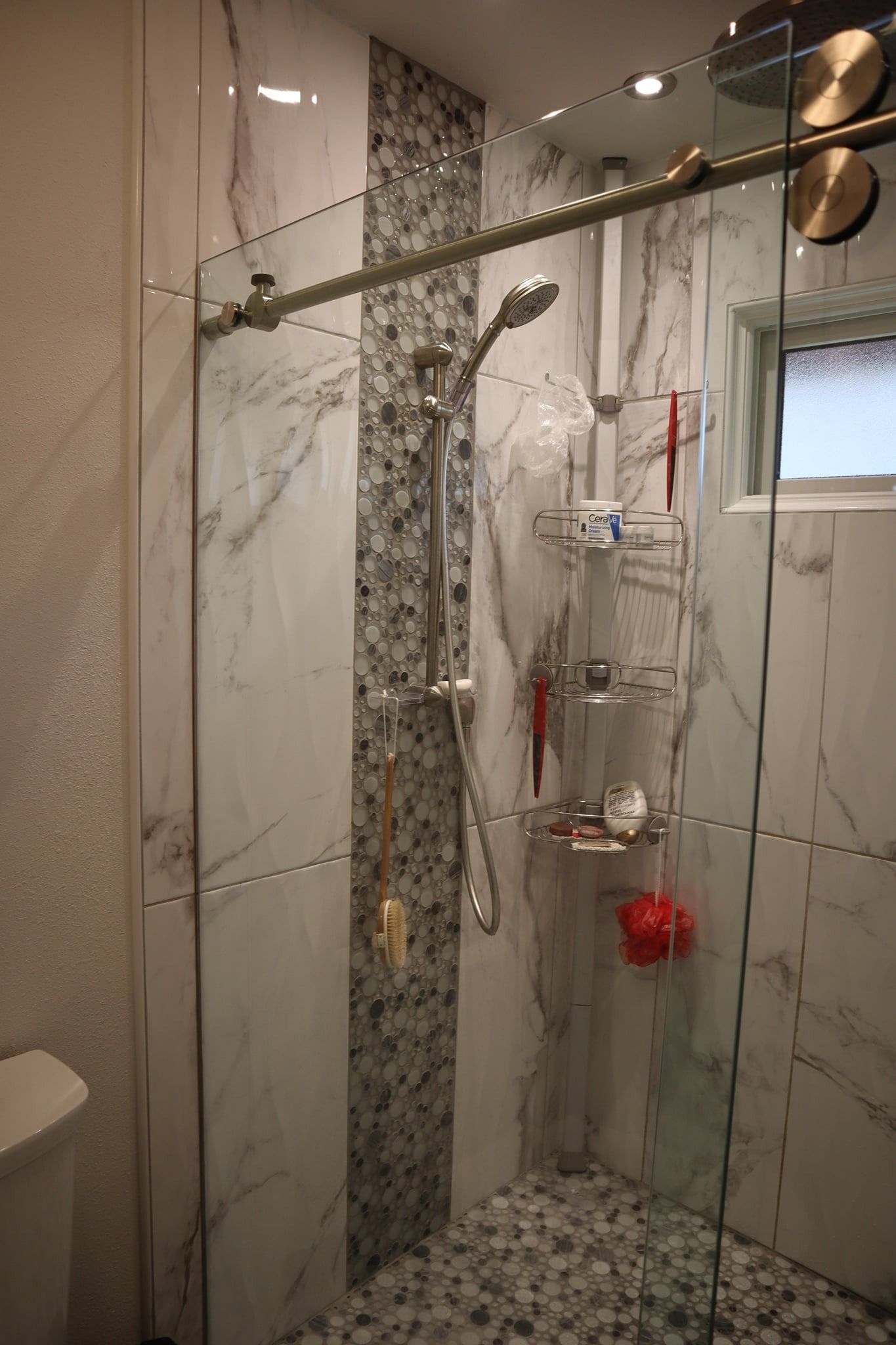 Shower with marble and pebble tile, glass doors, and shower accessories.