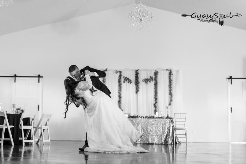 Couple dancing a wedding dip in a bright reception hall with a decorated table behind them