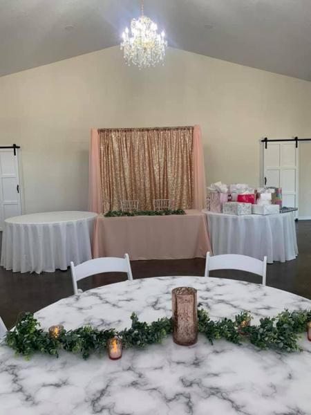 Decorated event room with white tablecloths, greenery, and a gold backdrop behind a central display table