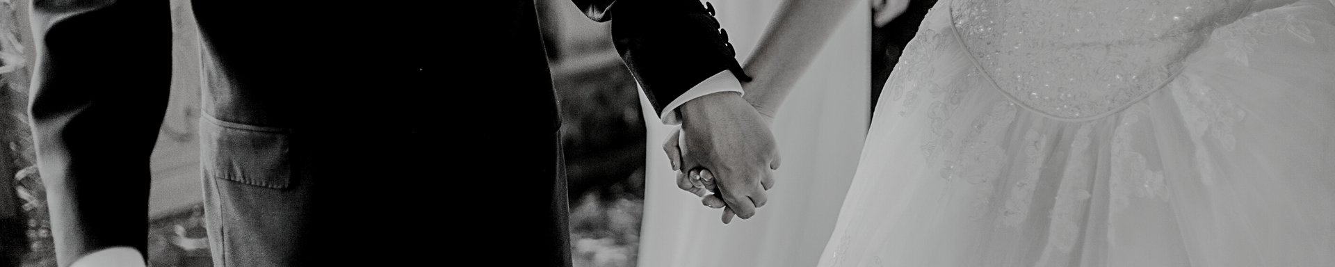 Two people holding hands, with a black suit on the left and a white dress on the right.