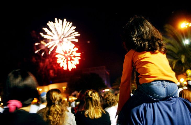 kid sitting on parents shoulders watching fireworks