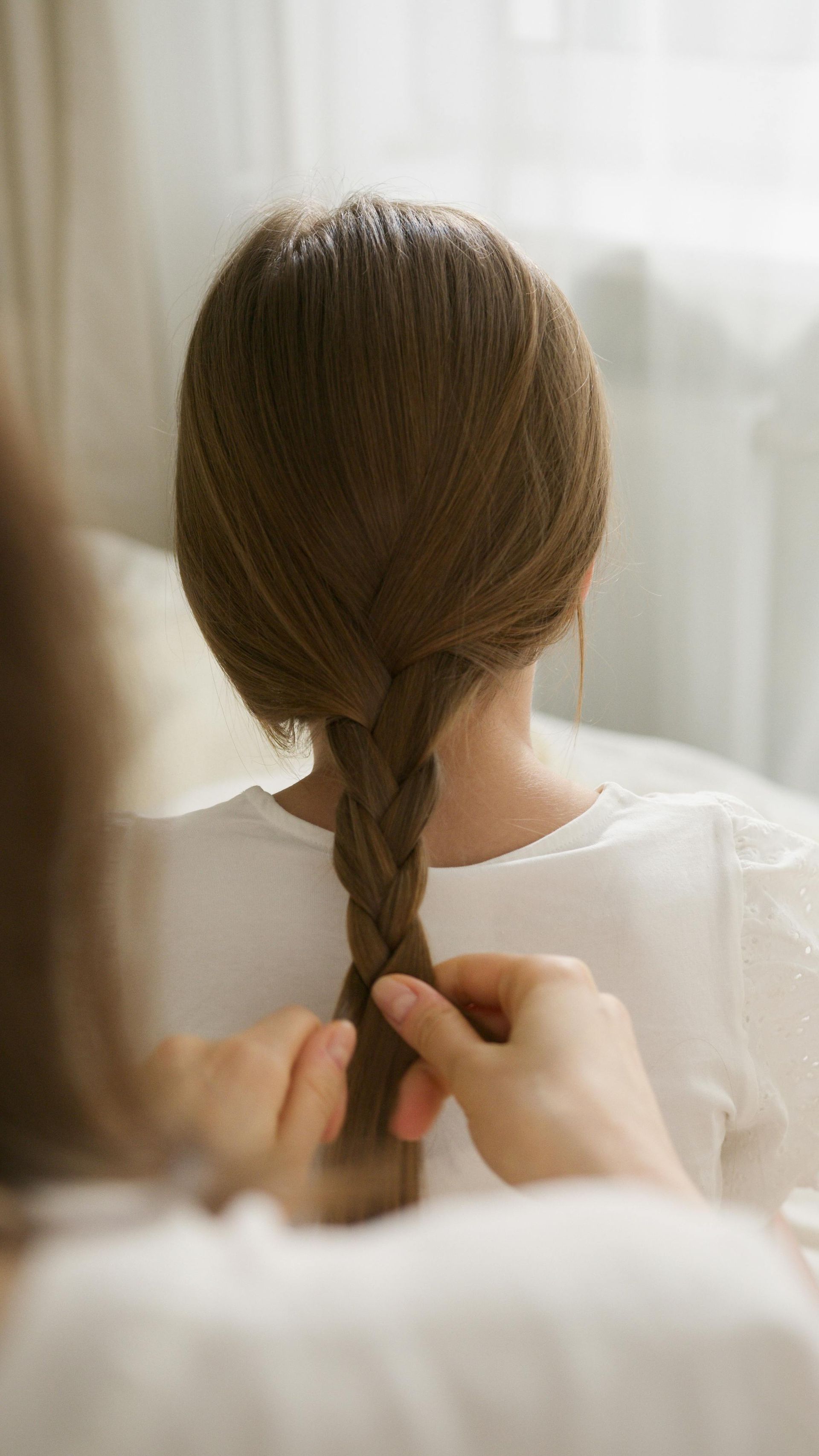 A woman is braiding another woman 's hair in front of a mirror.