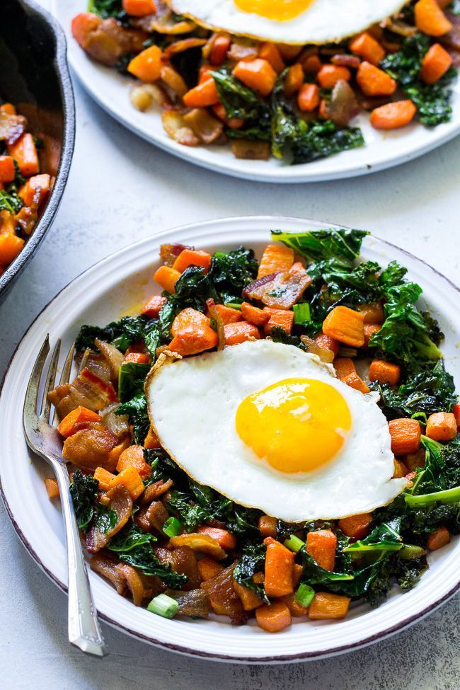 Two plates of sweet potato and kale hash, each topped with a sunny-side-up egg, next to a cast-iron skillet.