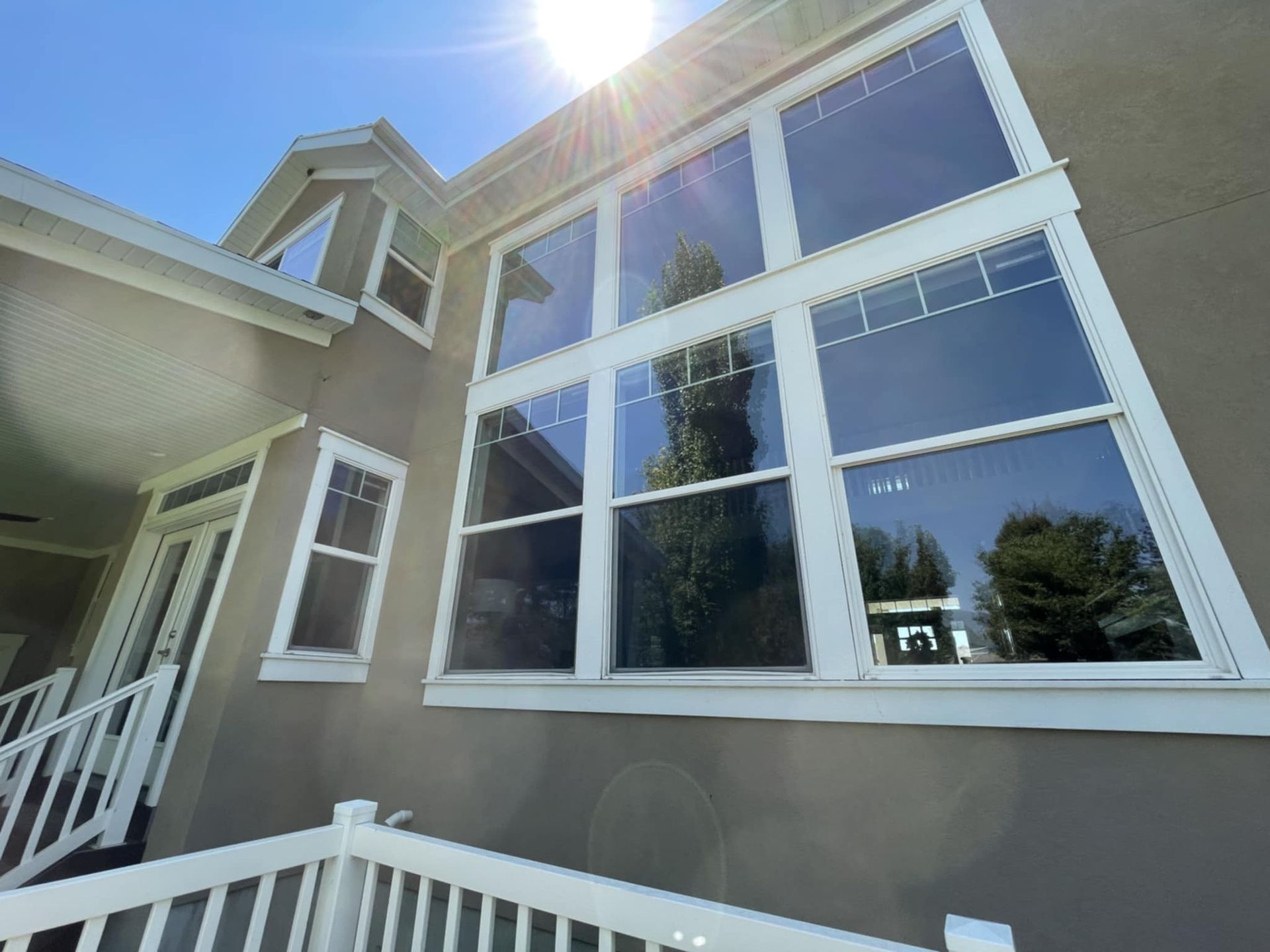 A large, tan house with white trim and large windows. The sun shines brightly in the sky.
