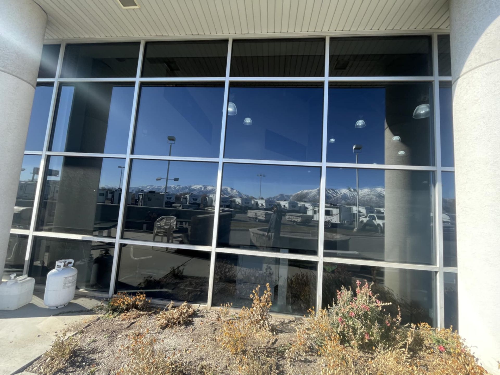 Large window reflecting a parking lot with mountains in the background; shrubs in front.