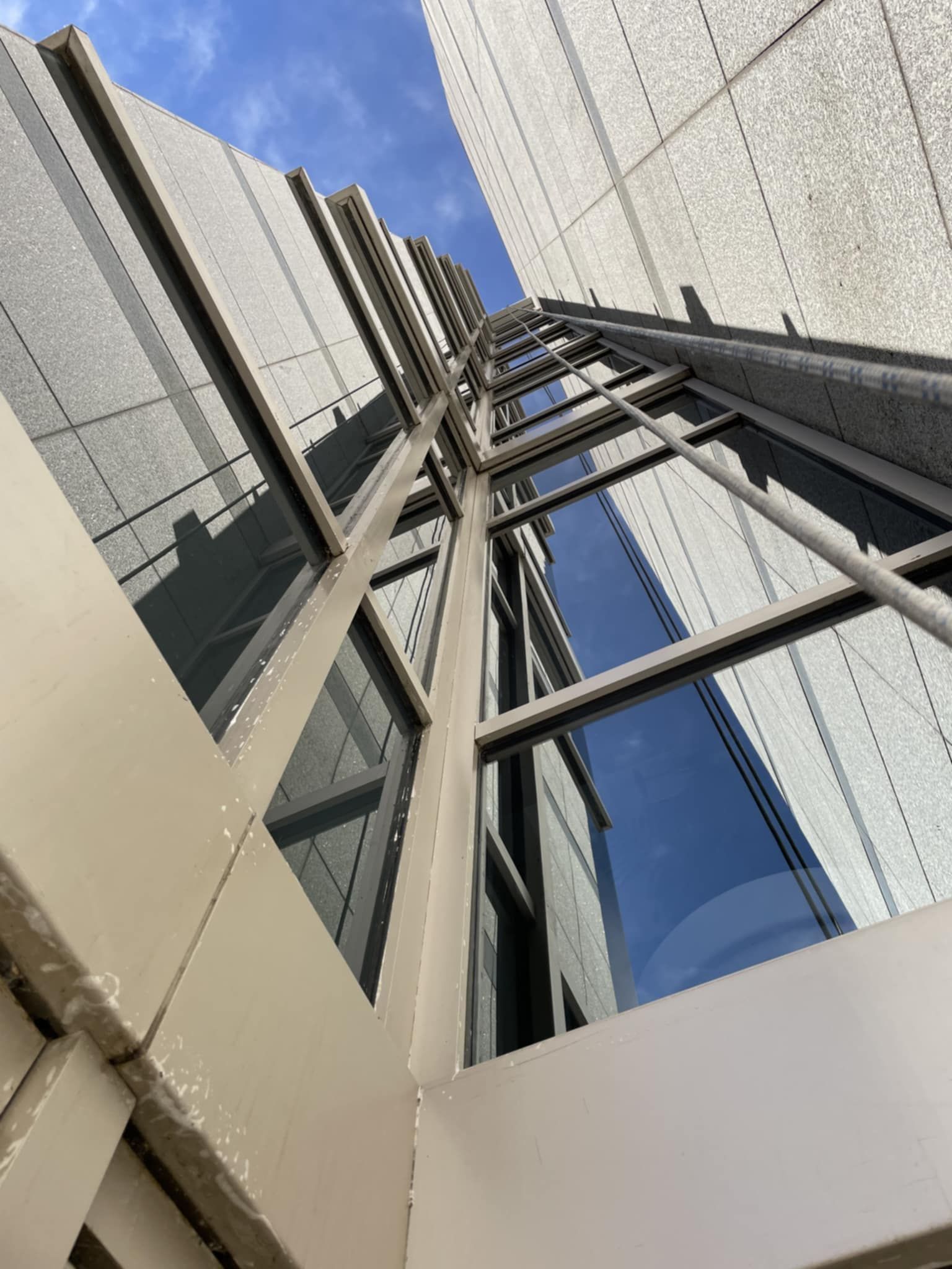 Low-angle view of a tall building with many windows reflecting the sky. The building has metal frames and a textured facade.