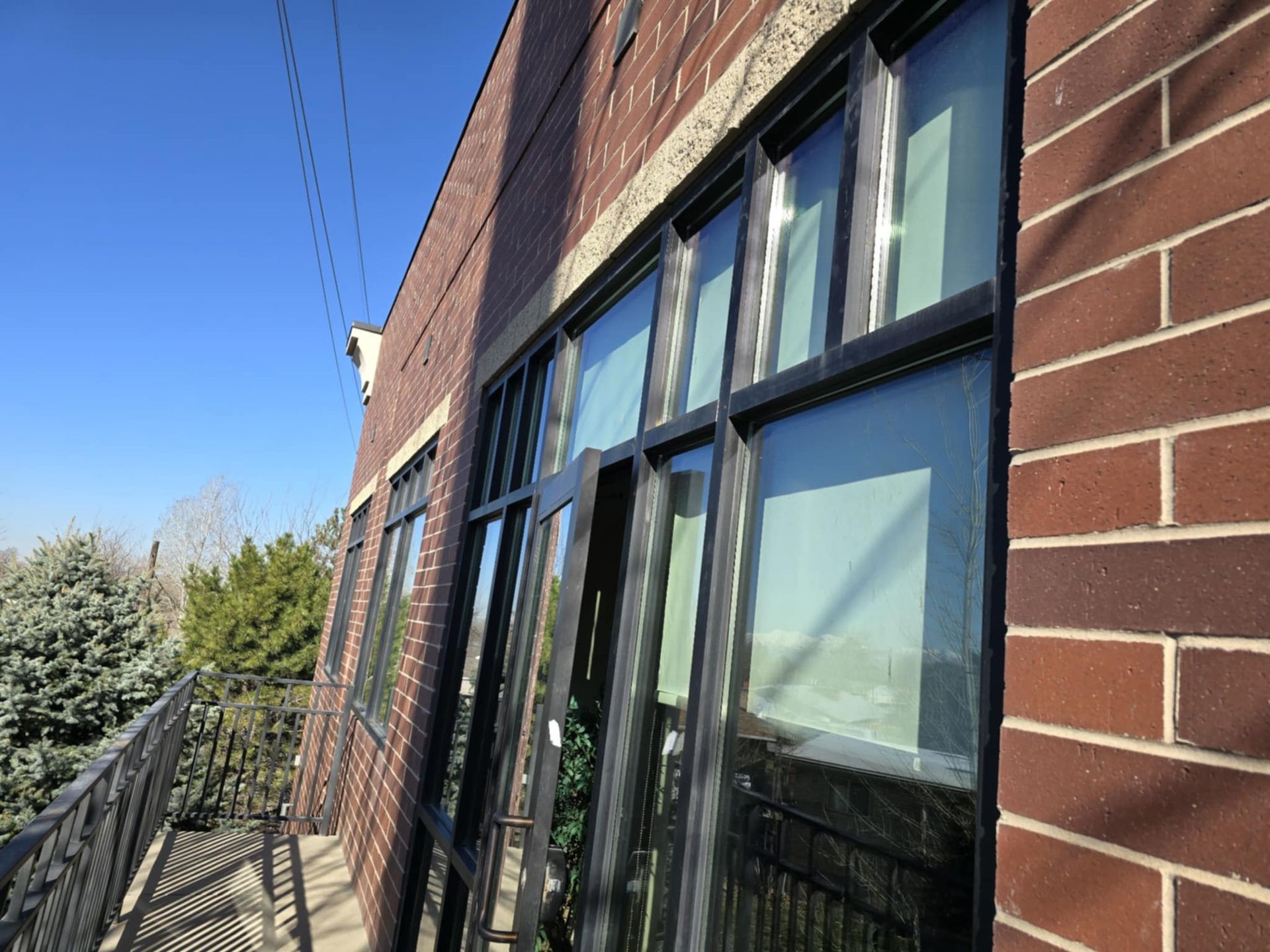 Red brick building with black-framed windows, some open, and a small balcony, against a blue sky.