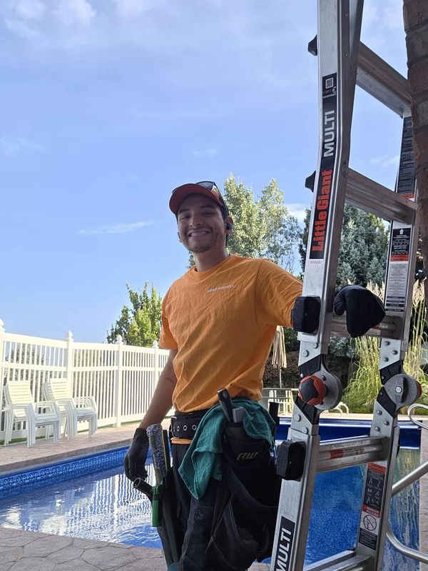 Man in orange shirt and cap by a ladder next to a swimming pool.