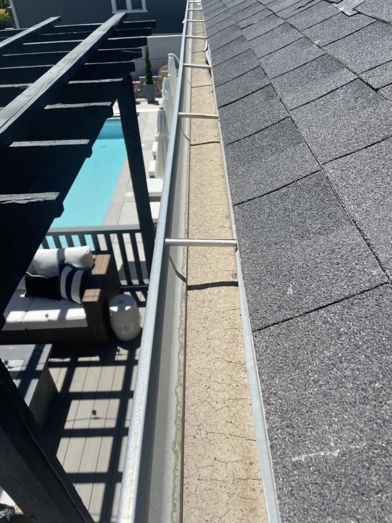 Gutter along a roof filled with debris, attached to a house overlooking a pool and patio.