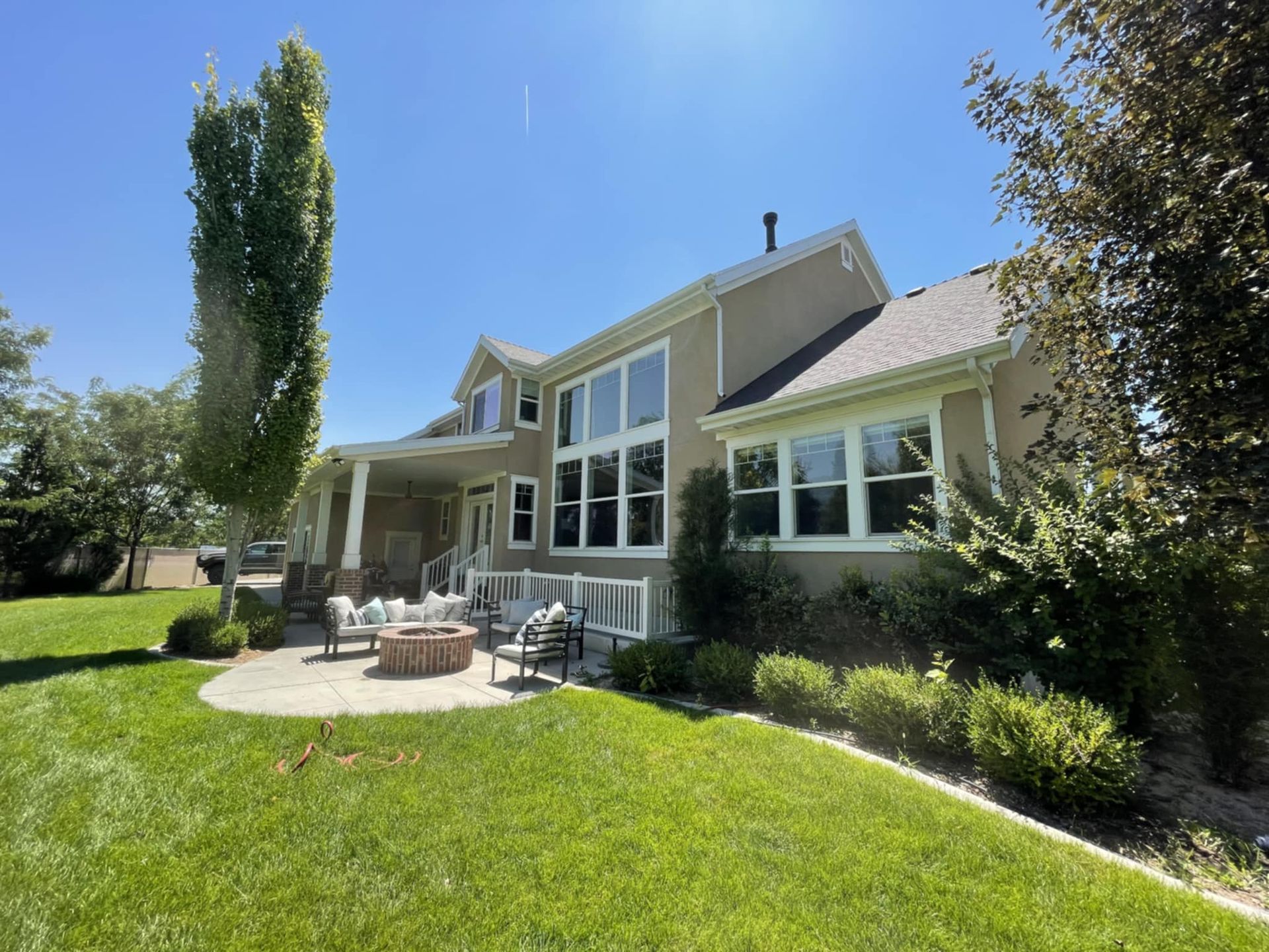 Beige house with many windows, patio with firepit, and green lawn on a sunny day.