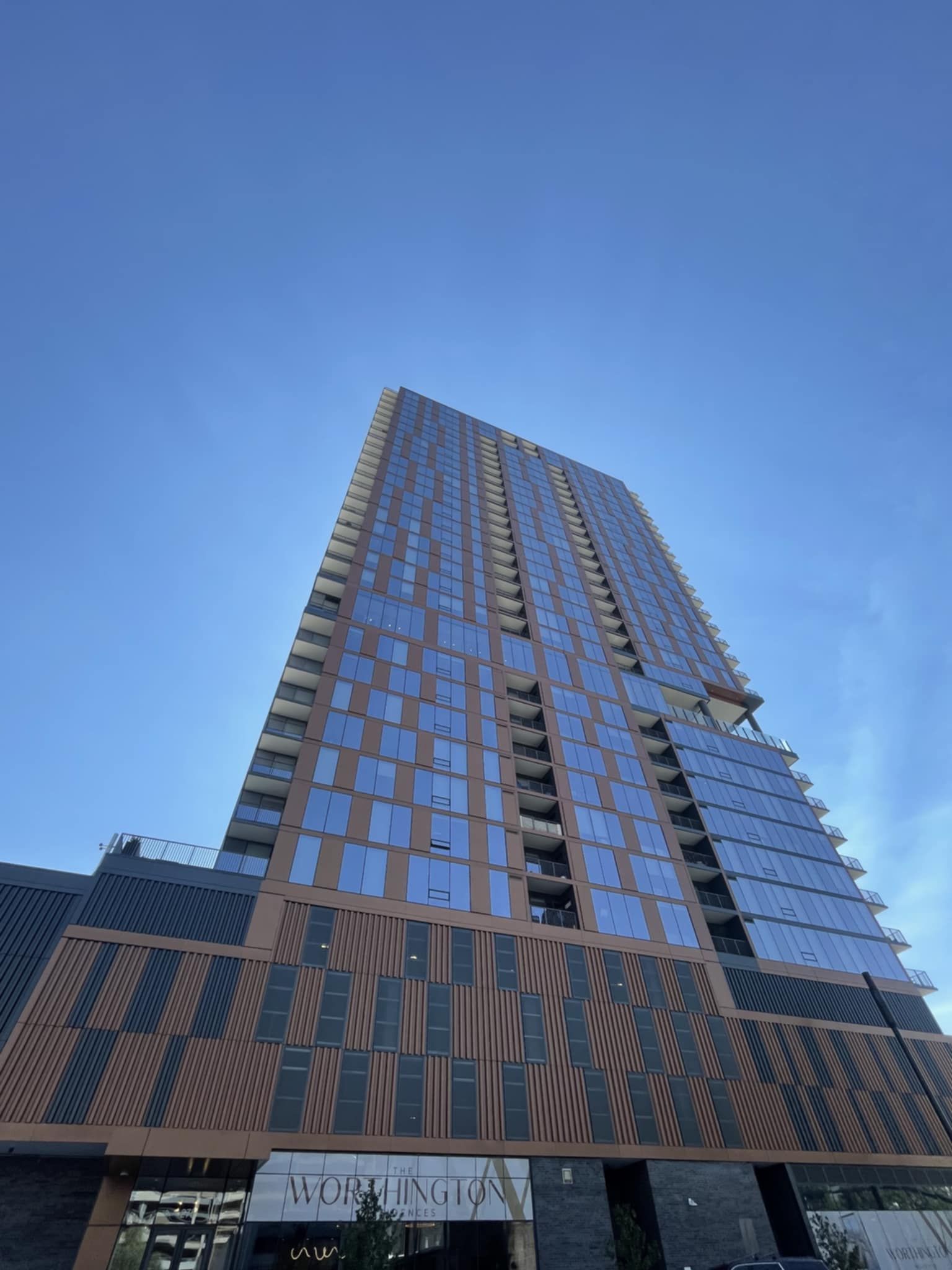 Tall modern building with blue glass windows and brown and black panels against a clear blue sky.