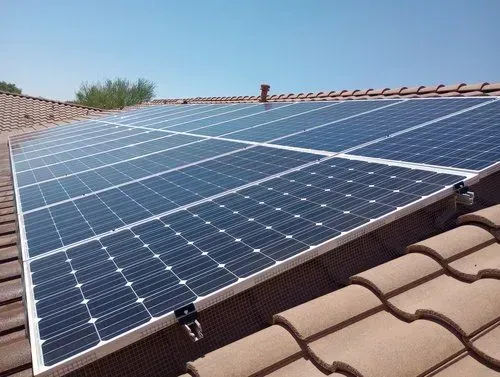 Solar panels installed on a terracotta tile roof against a blue sky.