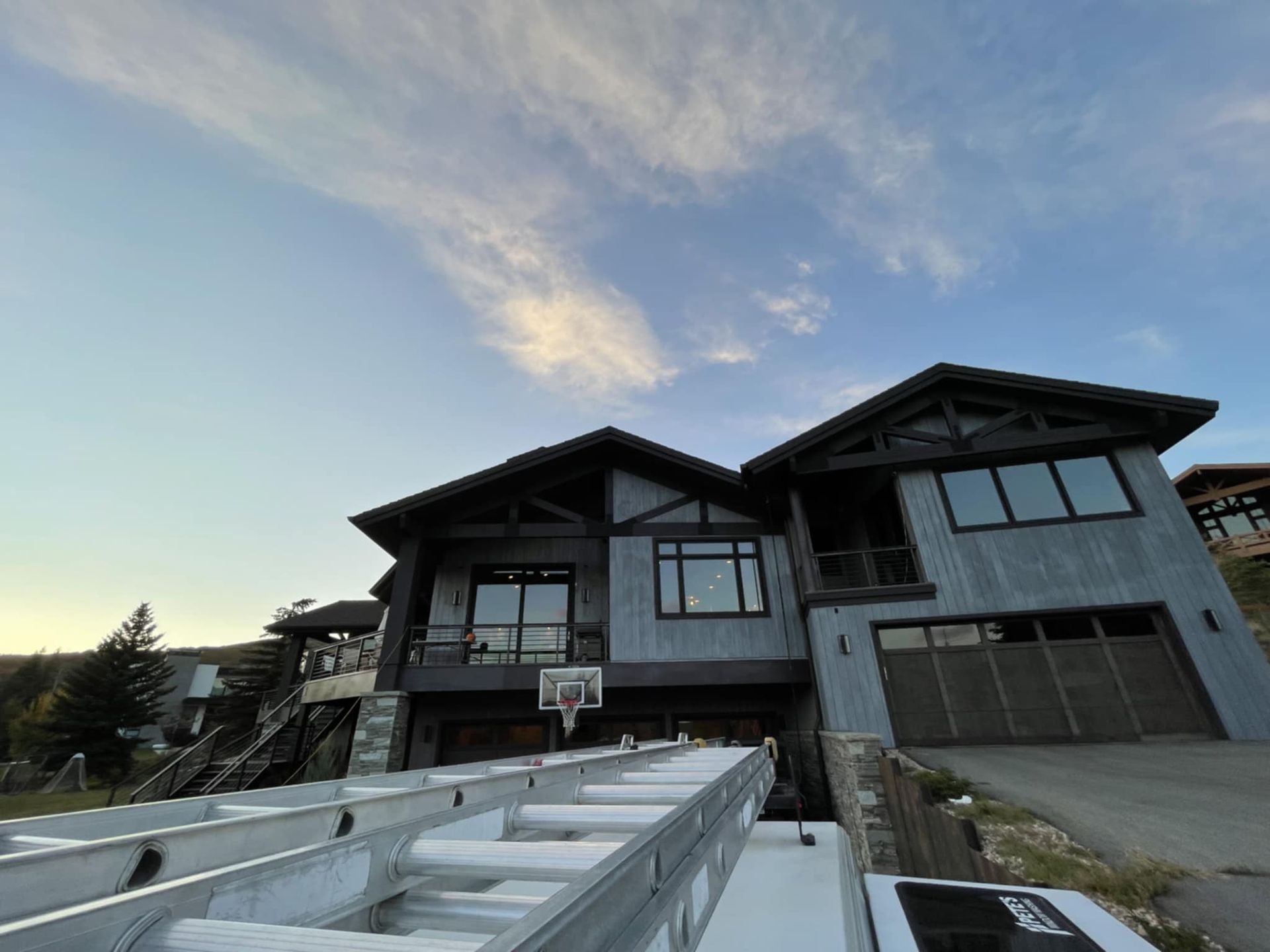 Two-story home with gray siding and brown trim under a cloudy sky. A ladder is in the foreground.