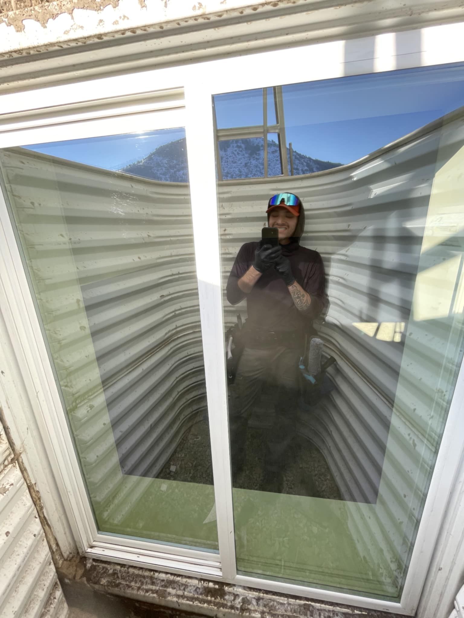 Person taking selfie in window well. Mountains reflect.