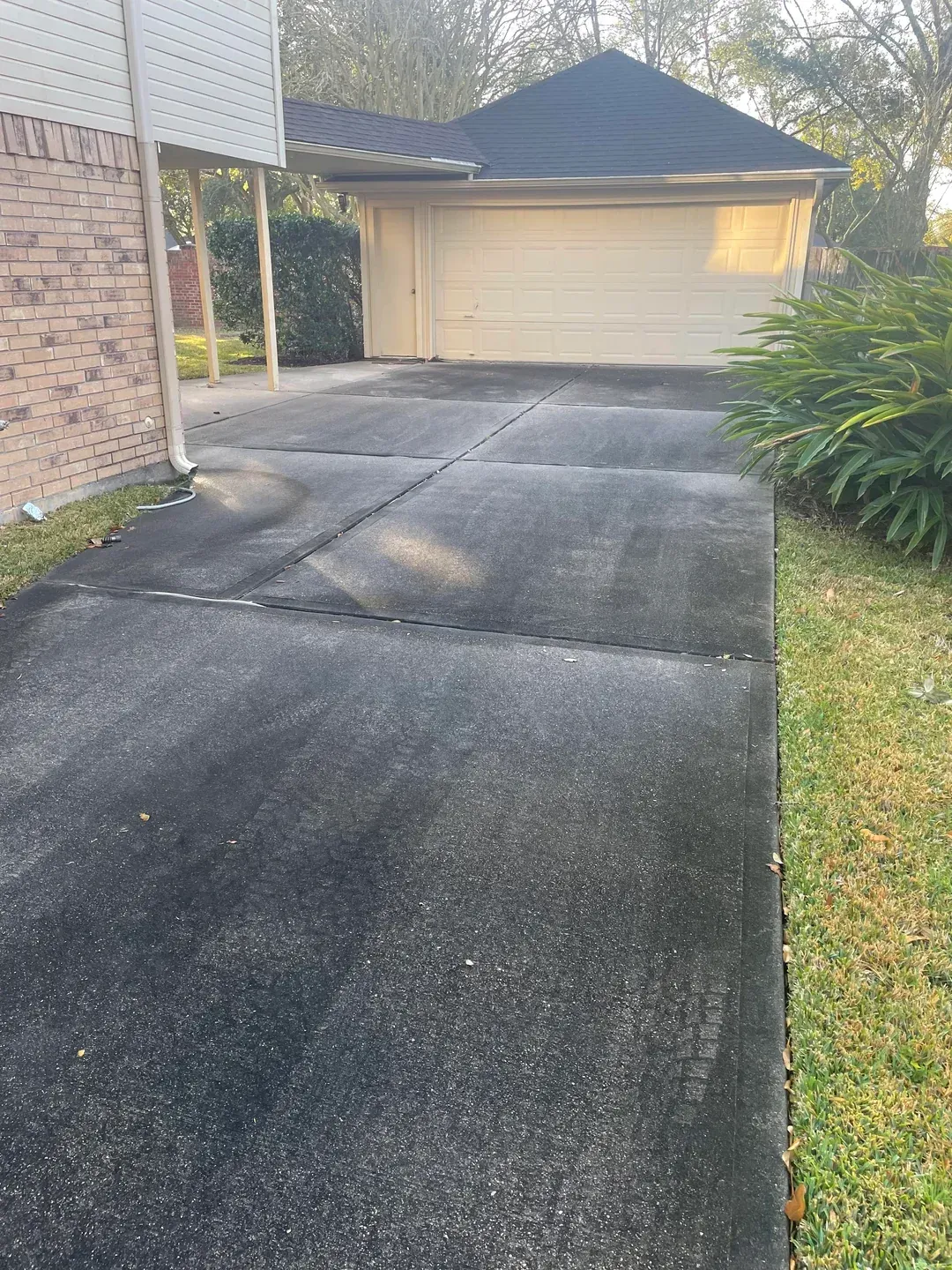 Black driveway leading to a beige garage, next to a brick building and grass.